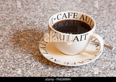 A large round cup of black coffee on a matching saucer with a spoon on a granite worktop Stock Photo