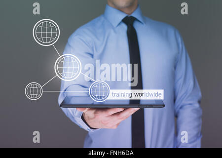 Businessman holding a tablet pc with worldwide training text on virtual screen. Internet and Business concept. Stock Photo