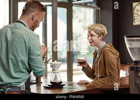 Friendly woman laughing with a barista in modern cafe Stock Photo