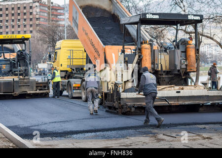 Workers next to paver asphalting road Stock Photo