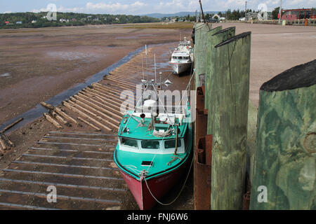 Fishing boats lie on harbour bottom beside the town pier at low tide in Parrsboro, NS Stock Photo