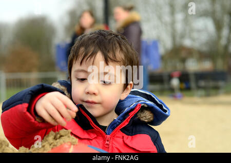 A young boy playing in a sand pit in the park. Stock Photo