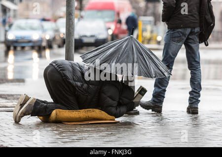 Homeless beggar is begging with umbrella in the rain near a walkway at a main street in Sofia. Bulgaria is one of the poorest co Stock Photo