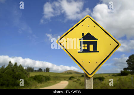 This way to buy the house of your dreams concept. Road sign with home icon in nature countryside landscape, includes copy space. Stock Photo