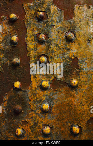 Grunge background with patterns and texture of weathered yellow paint on a rusty metal sheet with large rivets. Stock Photo