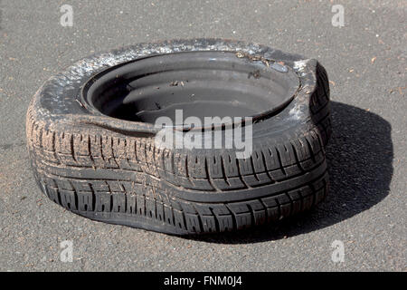 dirty deflated damaged tire on metal rim after blowout on road Stock Photo
