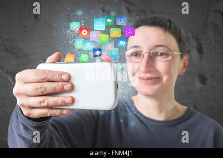 Woman holding a smart phone with modern colorful floating apps and icons. Selective focus. Stock Photo