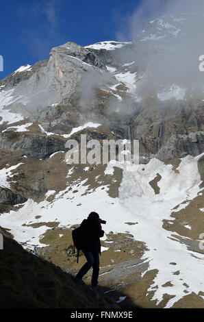 A man is taking a photographs on the steep slope in the mountain amphitheater de Troumouse. Stock Photo