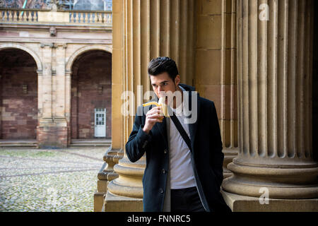 Young man with banana standing on street in Lausanne while looking down. Arch in sunlight on background Stock Photo