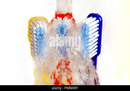 Water splashes over three differently coloured toothbrushes. Stock Photo