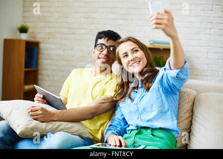 Smiling couple taking selfie while sitting on sofa Stock Photo