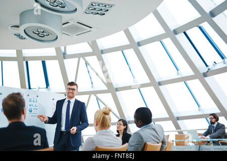 Smiling businessman pointing at whiteboard while presenting his ideas to business partners Stock Photo