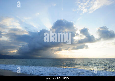 Sun ray clouds is lit brightly light golden seascape with waves rolling to the shore as scattered sunbeam breaks through. Stock Photo