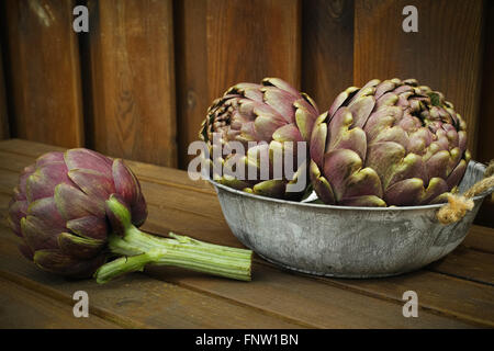 Fresh big Romanesco artichokes green-purple flower heads in tin bowl on wooden background Stock Photo