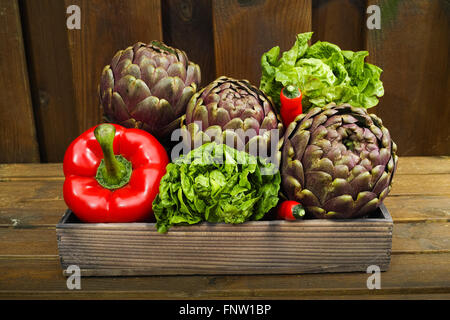 Fresh big Romanesco artichokes green-purple flower heads, red paprika, romanine lettuce on wooden background Stock Photo