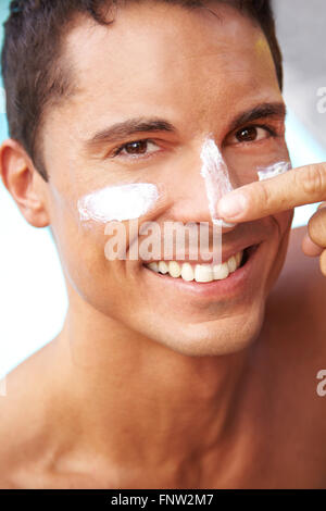 Happy smiling man putting sunscreen and suntan lotion on his face