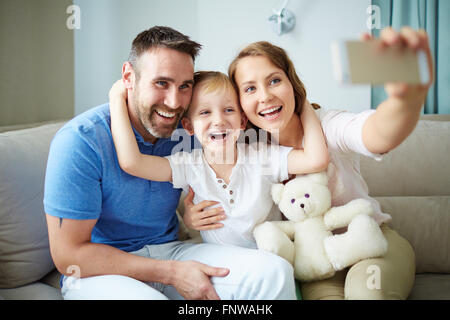 Family of three sitting on sofa and taking selfie Stock Photo