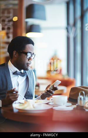 Elegant young man reading sms while eating in cafe Stock Photo