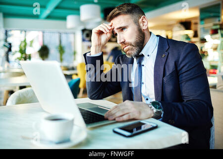 Pensive employee sitting in front of laptop by table Stock Photo