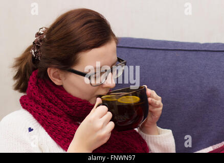 Sick woman wearing scarf lying in bed drinking tea Stock Photo