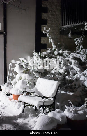 Night scene showing snow-covered seat in small patio garden in winter Stock Photo