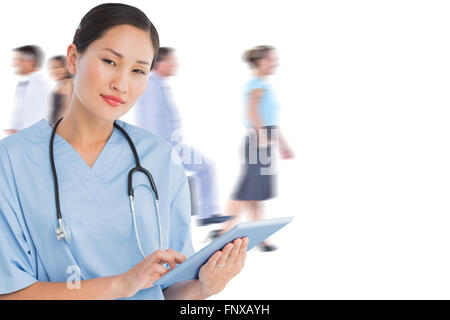 Composite image of surgeon using digital tablet with group around table in hospital Stock Photo