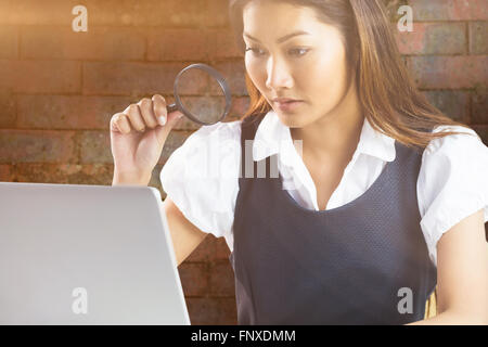 Composite image of businesswoman looking through magnifying glass and using laptop Stock Photo