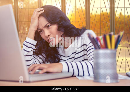 Composite image of concentrated asian woman with hand on head using laptop Stock Photo