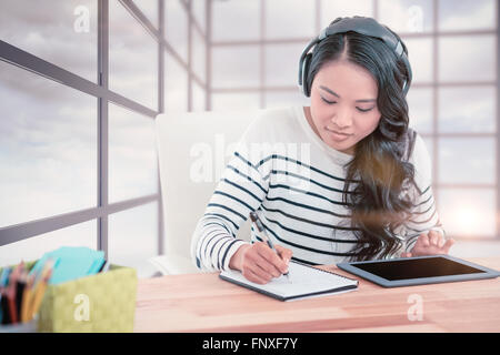 Composite image of smiling asian woman with headphones writing on notepad Stock Photo