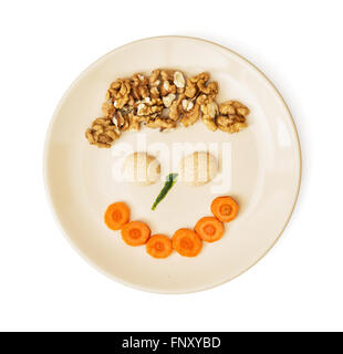 Funny face made of carrot, biscuits and walnuts on the plate. Crazy theme. Creative food. Stock Photo