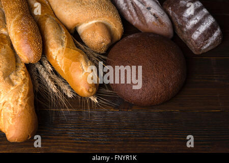 Group of rye and white artisan bread products piled over stalks of dried wheat on dark wooden table with copy space Stock Photo