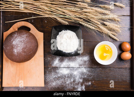 Top down view on baking ingredients of eggs, yolks, fine white flour, stalks of dried wheat and rye roll on top of cutting board Stock Photo
