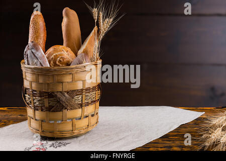 Rustic basket full of assorted fresh crusty bread from the bakery on an old wooden table with copy space behind Stock Photo
