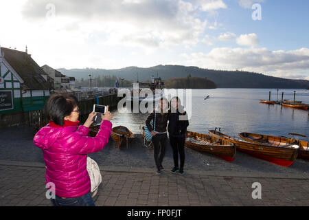 Lake Windermere, Cumbria, UK. 16th March, 2016. UK Weather: Lake Windermere -  Bowness Bay -Late aftrenoon -Last of the sun -Chinese tourist pose for picture with the tradtional rowing boats & thge steamer The Tern (Built 1891) in the background    Credit:  Gordon Shoosmith/Alamy Live News Stock Photo