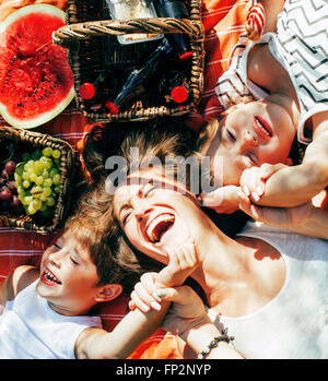 cute happy family on picnic laying on green grass mother and kids, warm summer vacations close up, brother and sister Stock Photo