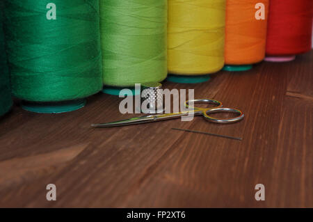 spools of thread for sewing and embroidery scissors, thimble, needle on background wooden table Stock Photo