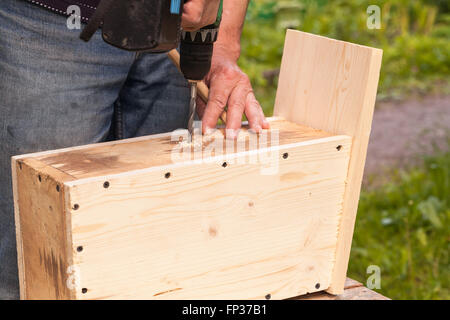 Wooden birdhouse is under construction, carpenter works with drill, closeup photo Stock Photo