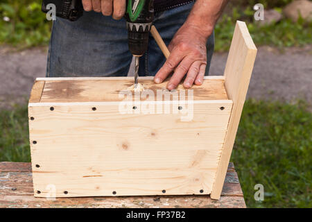 Wooden birdhouse is under construction, carpenter works with drill, close-up photo Stock Photo