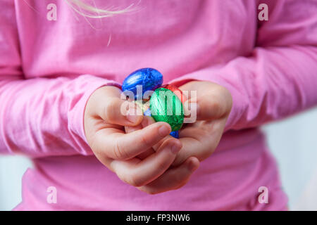 Child's hands holding chocolate Easter eggs wrapped in colorful foil with copy space Stock Photo