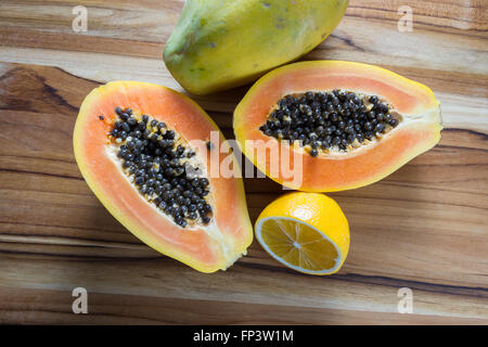 close up of a papaya cut in half on a wooden cutting board served with a sliced lemon Stock Photo