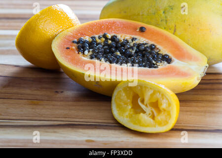 close up of a papaya cut in half on a wooden cutting board served with a sliced lemon Stock Photo