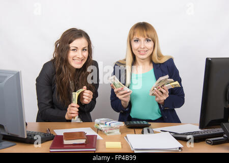 for office table two women collaborators happily hold hands in a pack with the money and express a strong admiration Stock Photo