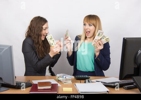 for office table two women collaborators happily hold hands in a pack with the money and express strong Stock Photo