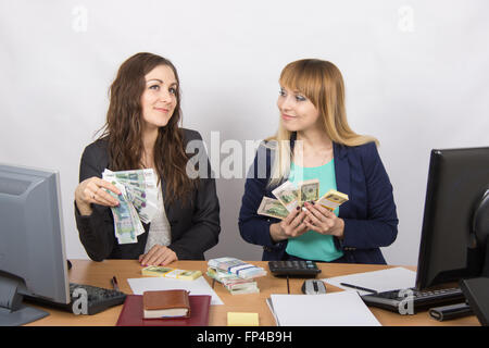 for office table two women collaborators happily hand-held fan of bundles of money, and discuss them dreamily Stock Photo