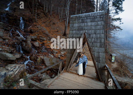 Wedding couple softly kiss on the wooden bridge. Misty day in mountains Stock Photo