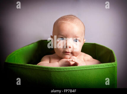 Portrait of a cute 3 months baby boy sitting in a green box for toys Stock Photo