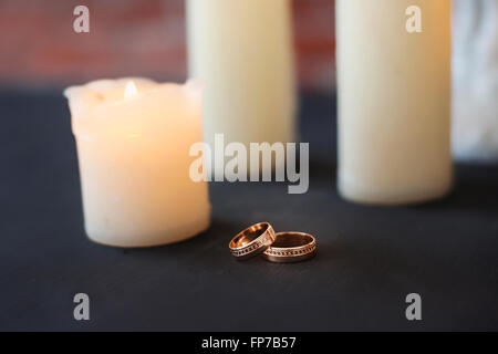 Old white candles on old black table at red brick wall background. Stock Photo