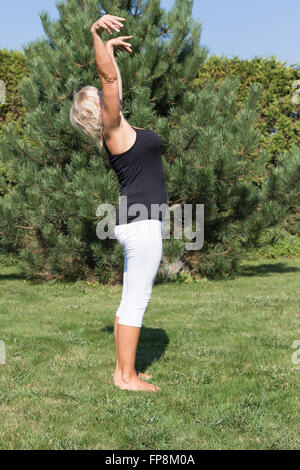 Blonde senior woman is exercising standing on the lawn outside. Stock Photo