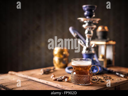 Still life of black tea in glass cup on wooden table, hookah in background Stock Photo