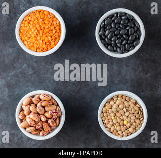 Red and brown lentils, heirloom beans, and black turtle beans on dark grungy surface. Top view with copy space. Stock Photo